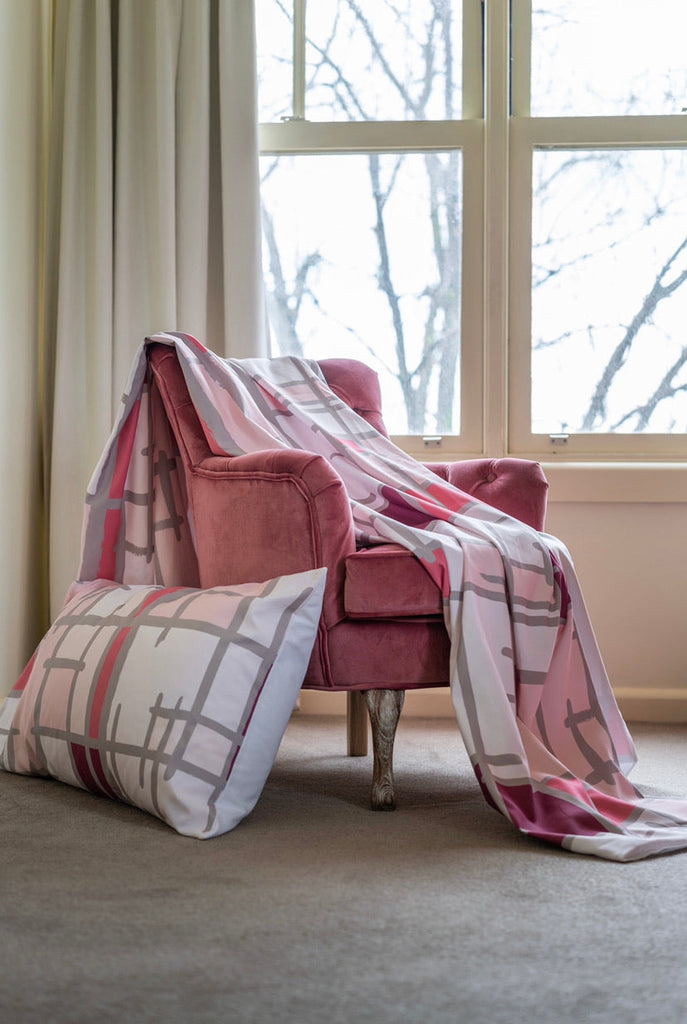 Pink quilt cover layed out over a pink velvet chair.  In the background is a light filled window.